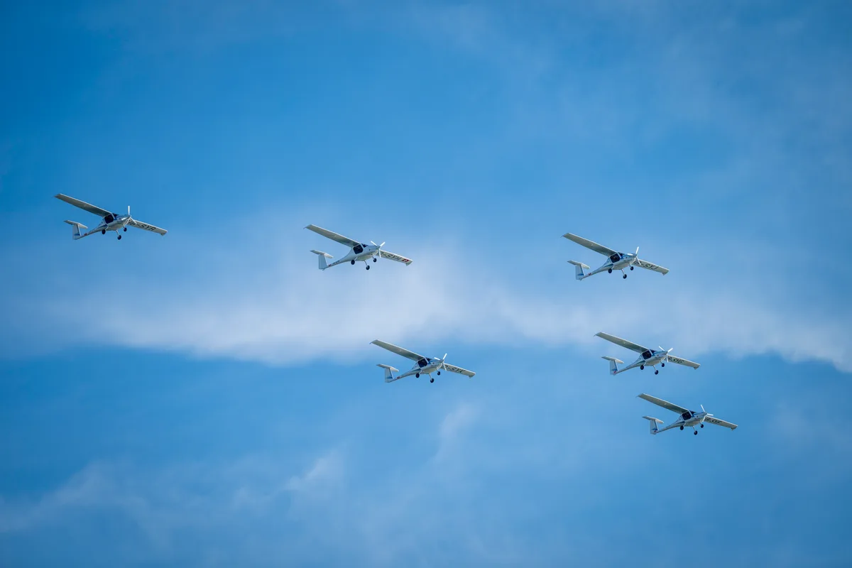 Hier ist Koordination gefragt: Die E-Flugzeuge flogen in Formation über das Festgelände. Mehrere Propellerflugzeuge am Himmel.